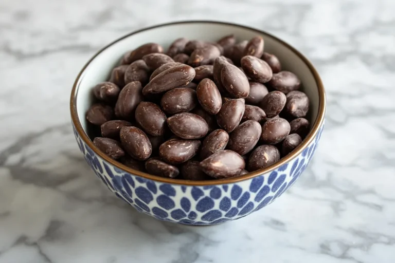 Dark chocolate almonds in a white bowl on a wooden table.